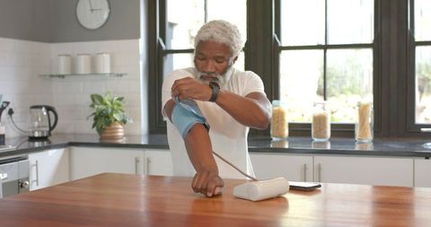 Senior man using digital blood pressure monitor in modern kitchen