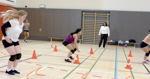 Volleyball players practicing cone agility drill in indoor gym with coach supervising