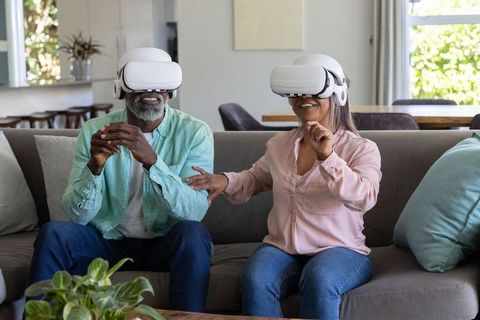 Mature couple exploring virtual reality together at home using white vr headsets
