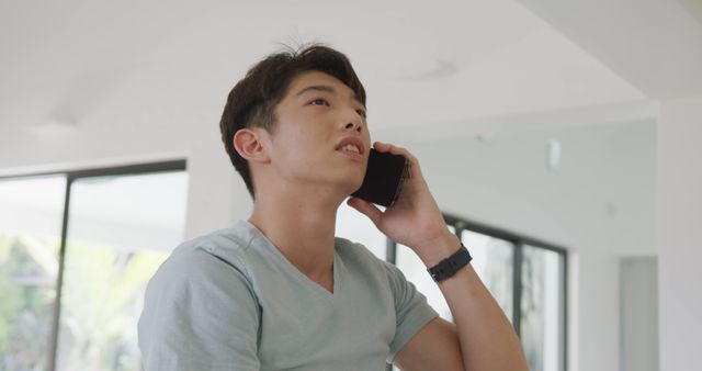 Asian male teenager talking on smartphone and smiling in living room. spending time alone at home.