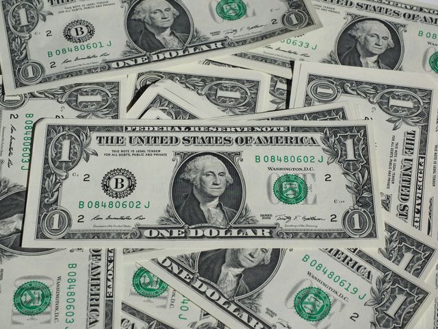 Multiple one dollar bills appear scattered, creating a textured financial background. Useful for themes involving finance, wealth management, banking, economic studies, and financial planning materials.