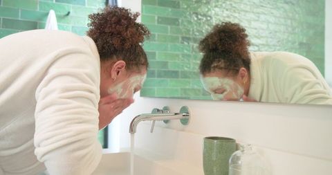 African american woman washing face at sink with foamy cleanser in modern bathroom
