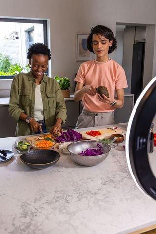 Diverse friends chopping vegetables and preparing salad at kitchen island with ring light
