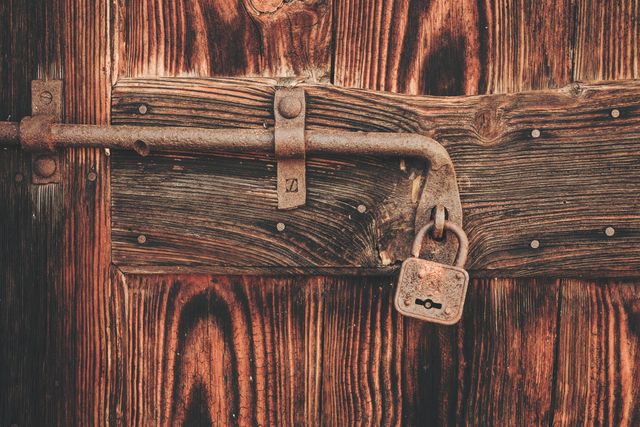 The image presents a close-up view of a rustic wooden door featuring a weathered, rusted lock and latch mechanism. Ideal for use in themes of security, history, or vintage aesthetics. Suitable as visual content in blogs, articles, advertisements, or decor ideas relating to historical places, antique craftsmanship, or traditional architecture.