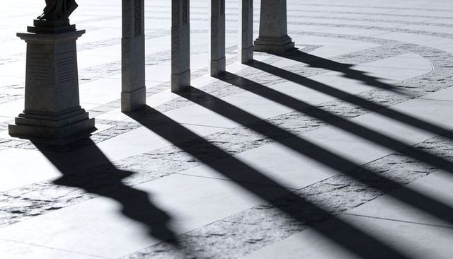 Sunlit columns casting long diagonal shadows across patterned marble plaza