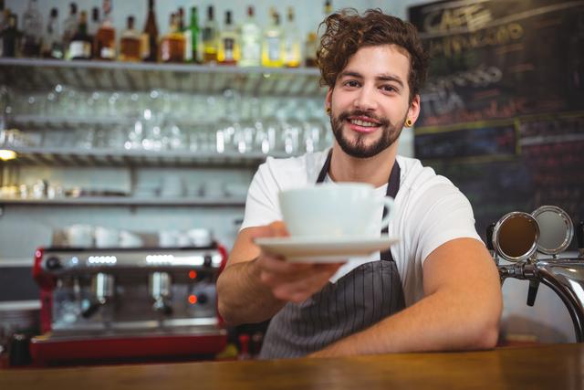 Portrait of smiling waiter serving a cup of coffee at counter in cafÃ©