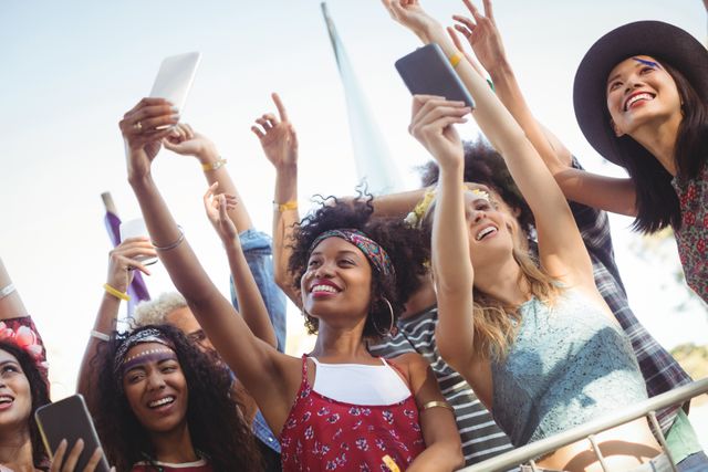Group of friends enjoying a music festival, capturing memories with their mobile phones. Perfect for use in promotions for music festivals, summer events, youth culture, and social media campaigns.