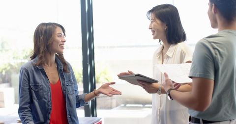 Diverse coworkers collaborating with tablet and documents near desk