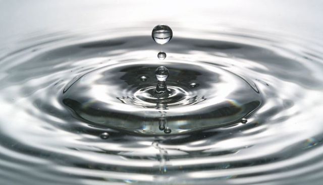 Capturing water droplet creating crown and concentric ripples on reflective surface
