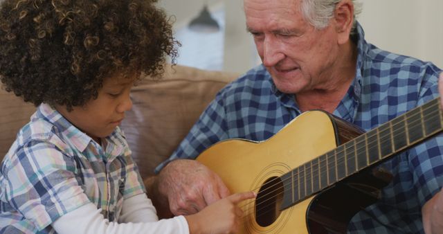 Image of biracial grandson and caucasian grandfather playing the guitar together. Family life, spending time together with family.