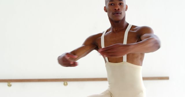 African American male ballet dancer dressed in a beige costume performing an elegant dance move in a studio. This can be used for promoting artistic activities, dance classes, fitness programs, or inspirational content about professional dancers.
