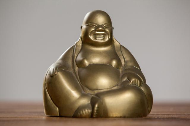 Gold Laughing Buddha figurine sitting on a wooden table, symbolizing prosperity and happiness. Ideal for use in home decor, spiritual spaces, meditation rooms, or as a feng shui element to bring tranquility and positive energy.