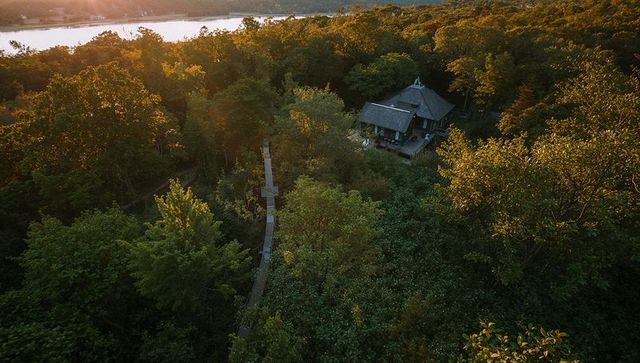 Sunlit riverside cabin with raised boardwalk through forest canopy at golden hour