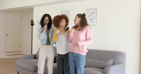 Diverse female friends singing karaoke in living room with microphones, casual home fun