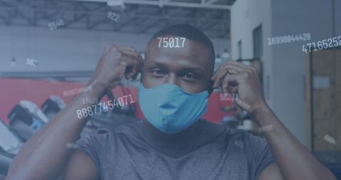 Man Putting on Face Mask in Gym with Floating Numbers