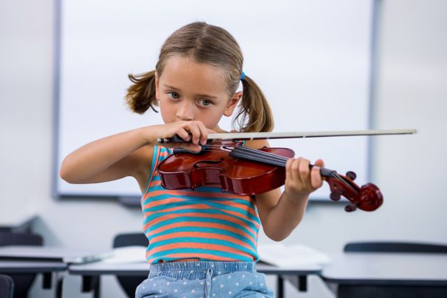 Girl playing violin against whiteboard in classroom