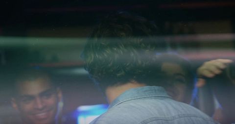 Friends chatting inside car at night through reflective window with denim shirt and neon flare