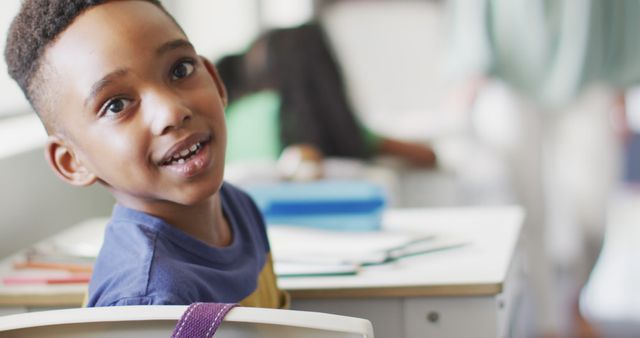 Image of happy african american boy sitting at desk during lesson in classroom. primary school education and learning concept.