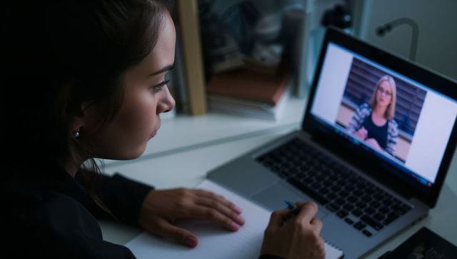 Young woman studying during online lecture at home desk with laptop and notebook