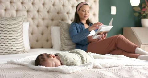 Mother Reading While Baby Sleeps on Bed in Cozy Home Interior