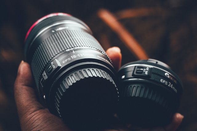 Close-up view of two camera lenses being held in hand, showcasing different millimeter ranges. Suitable for photography, technology, and camera equipment themes. Ideal for articles, blog posts, or advertisements related to photography, camera reviews, or tech accessories.