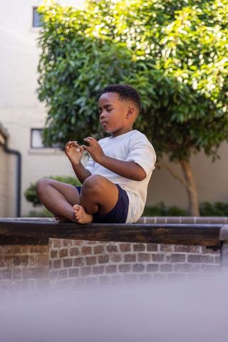 African american child sitting meditating on brick ledge barefoot sunlit courtyard