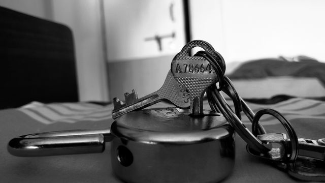 Detailed monochrome close-up of a metal lock with attached keys on a table. Ideal for illustrating security, protection, privacy, or the concept of solution and access. Perfect for blogs, articles, and security-related materials.
