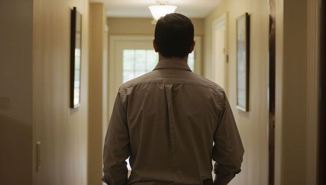 Man walking down narrow home hallway wearing button-up shirt with rolled cuffs