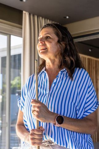 Woman holding pool cue in bright game room wearing striped shirt and smartwatch