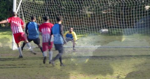 Amateur soccer players chasing goal while goalkeeper diving on muddy local pitch