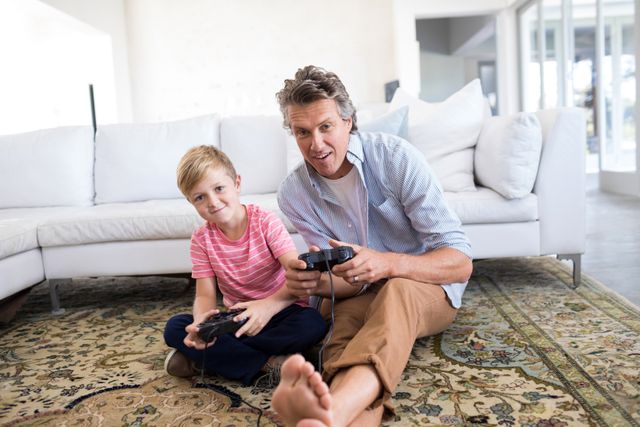 Father and son enjoying quality time together playing a video game in a bright living room. Ideal for use in family-oriented content, parenting blogs, advertisements for gaming consoles, or articles about family bonding and leisure activities.