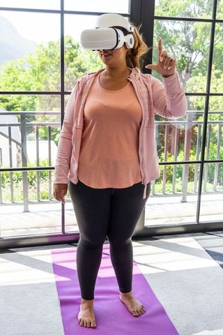 Woman practicing vr fitness at home on yoga mat wearing headset and making gesture