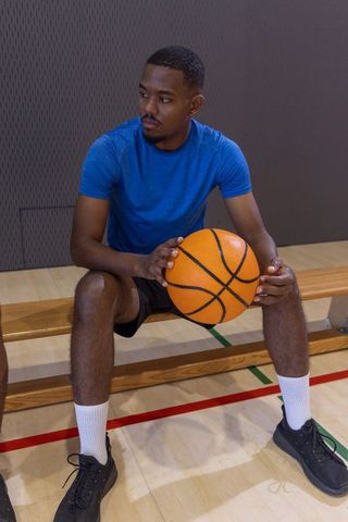 African american basketball player sitting on bench holding ball looking focused in gym