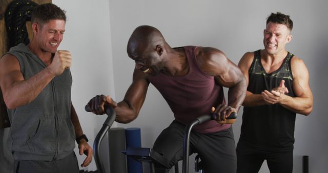 Group of men motivate each other while exercising inside gym. One man intensely cycles on a stationary bike while the others cheer. Ideal for use in fitness magazines, motivational posters, gym advertisements, and exercise blogs to promote teamwork and group workouts.