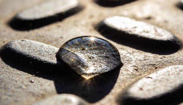Closeup macro water droplet refracting textured metal studs with gold starburst highlight