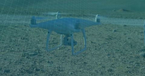 Quadcopter drone hovering over barren landscape with grid overlay