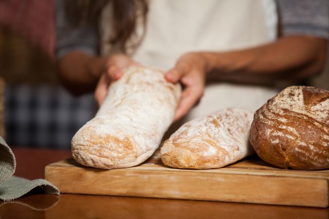 Woman holding freshly baked bread at a market counter. Ideal for use in articles or advertisements related to baking, artisan bread, farmers markets, and homemade food. Can be used for promoting bakery products, recipes, and culinary blogs.