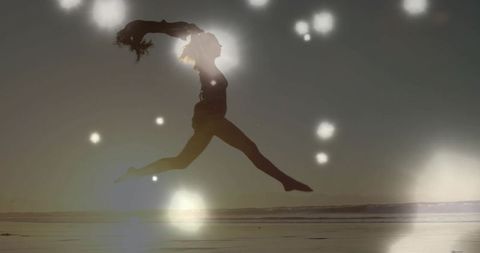 Backlit female dancer performing split leap over wet beach at sunset with silhouette