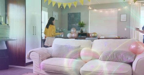 Woman walking carrying bowl toward decorated living room with pastel balloons and bunting