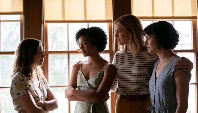Supportive group of friends standing by sunlit window having reflective conversation