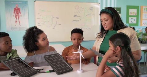 African american teacher guiding kids using solar panels and wind turbine for stem learning
