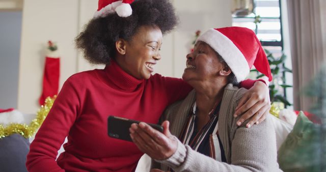 Happy african american mother and adult daughter in christmas hats using smartphone, slow motion - Download Free Stock Photos Pikwizard.com
