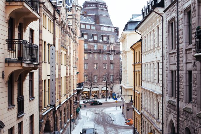 Captivating view of a European street with historic architecture during winter. Buildings covered in snow, creating a picturesque and serene urban atmosphere. Ideal for travel brochures, tourism websites, architectural studies, and winter-themed marketing materials.