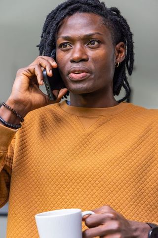 African american man talking on smartphone holding white coffee mug, casual workspace moment