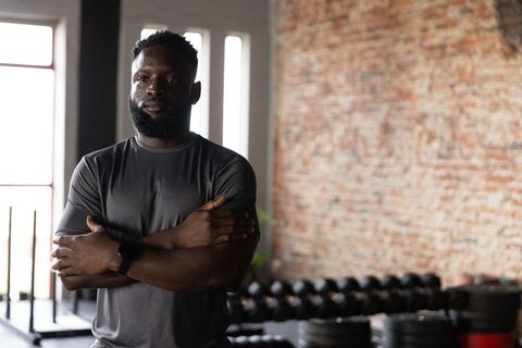 African american athlete standing arms crossed wearing smartwatch projecting confidence in gym
