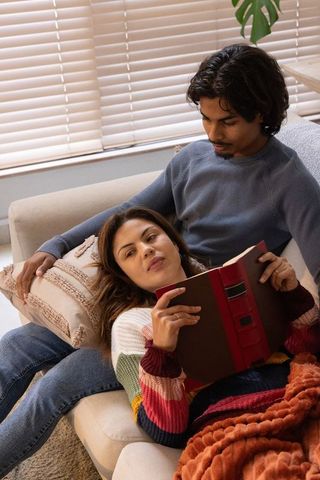 Diverse couple relaxing on sofa while reading hardcover book