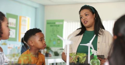 Teacher guiding students through renewable energy project with wind turbines and seedlings