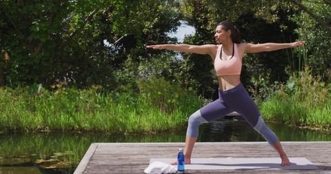 Woman practicing yoga on outdoor jetty by forest river