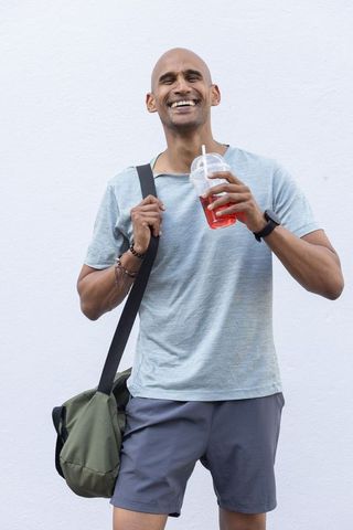 Smiling african american man holding red drink wearing gym shorts and duffel bag