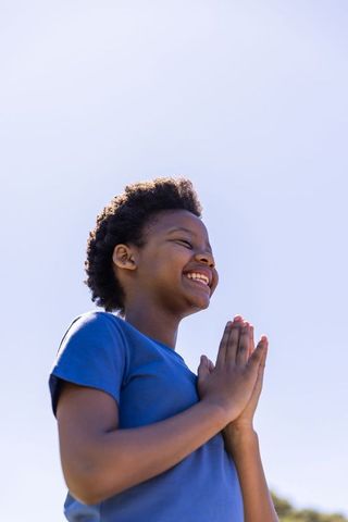 African american boy smiling with hands pressed in gratitude outdoors bright sky